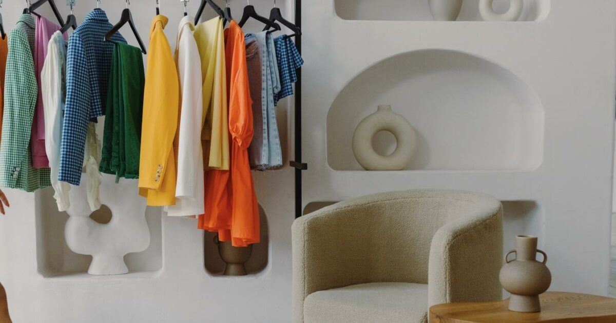 A Woman Is Standing In Front Of A Rack Of Clothes, Contemplating What To Wear For Her Photoshoot.