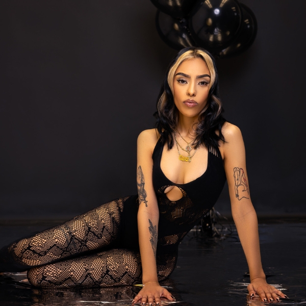 A Woman In A Black Bodysuit Posing On The Floor.