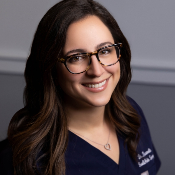 A Smiling Woman In Glasses Wearing A Scrub Shirt.