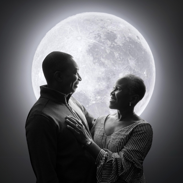 A Couple Standing In Front Of A Full Moon.