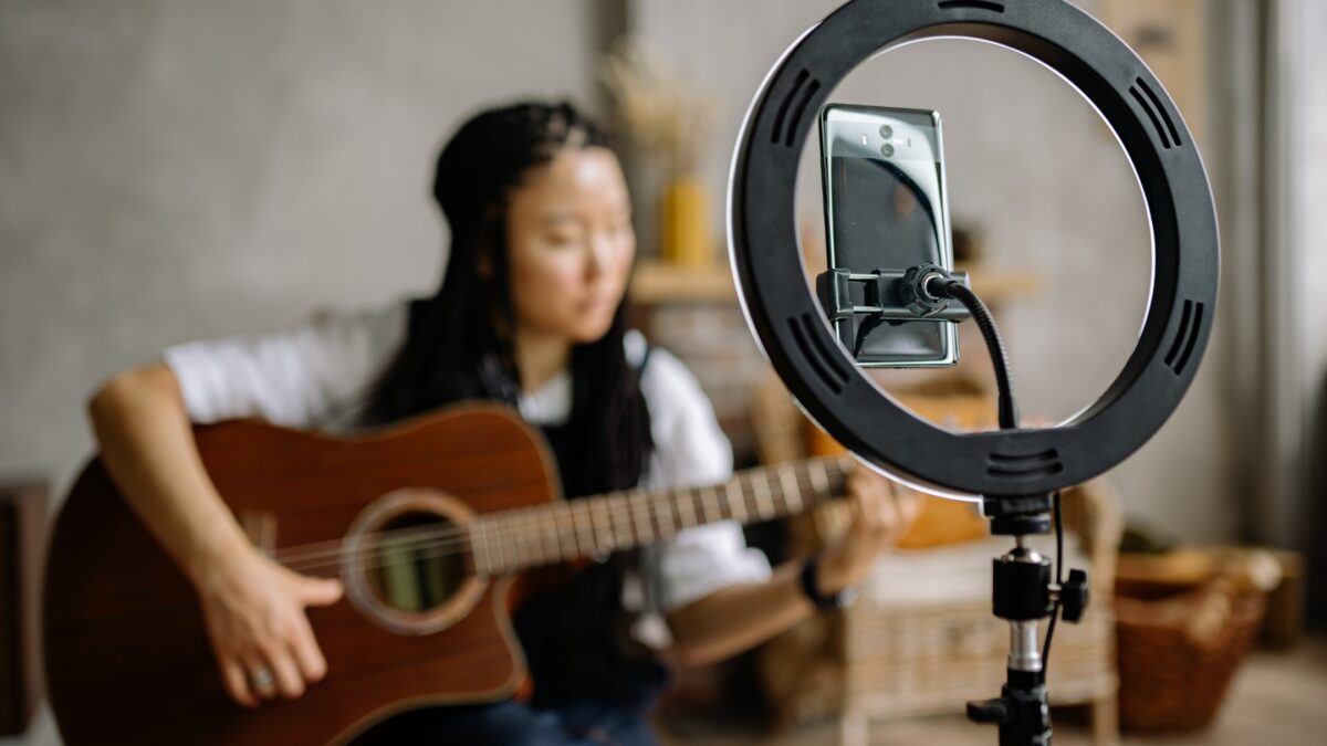 A Woman Strumming An Acoustic Guitar While Illuminated By A Ring Light For Photography.