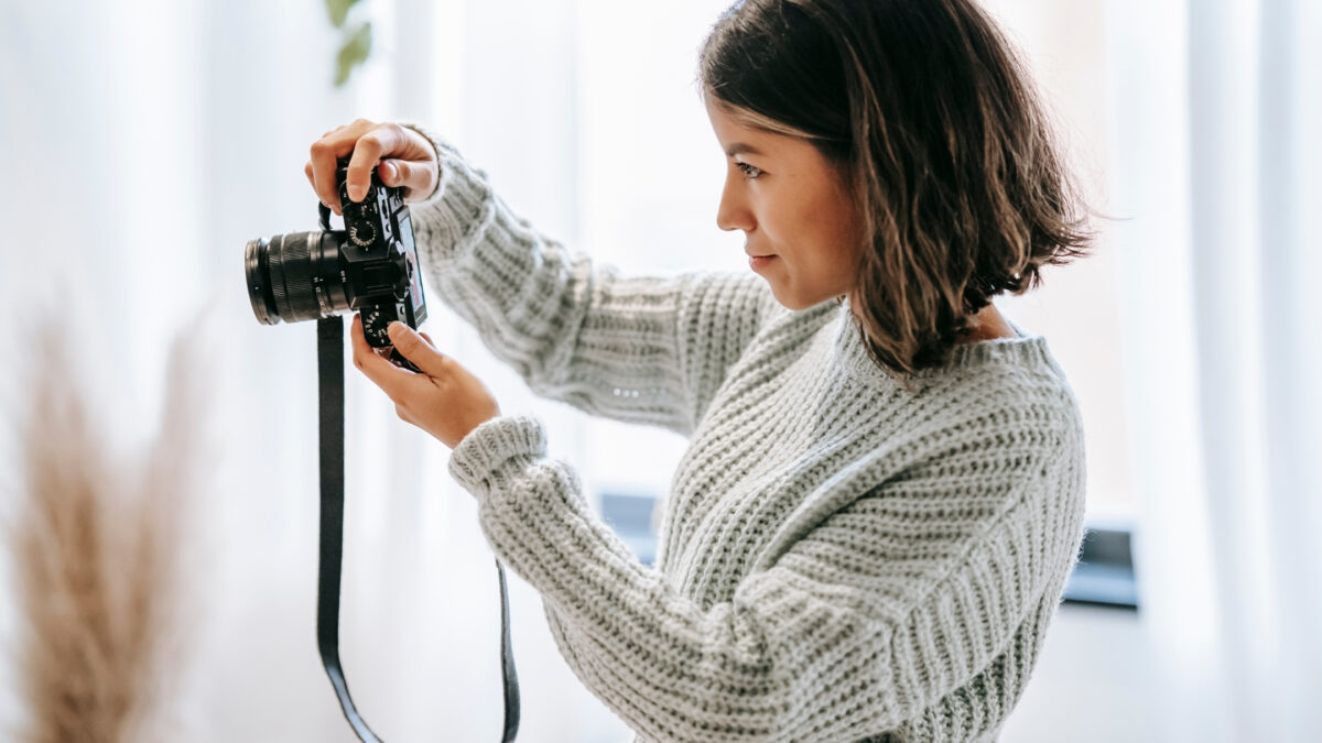 A Woman Capturing Feedback On Photos With A Camera In Front Of A Window.