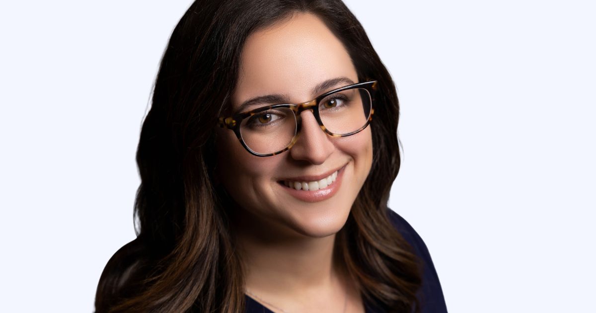 A Woman Wearing Glasses Smiles In Front Of A White Background, Captured In Photography.